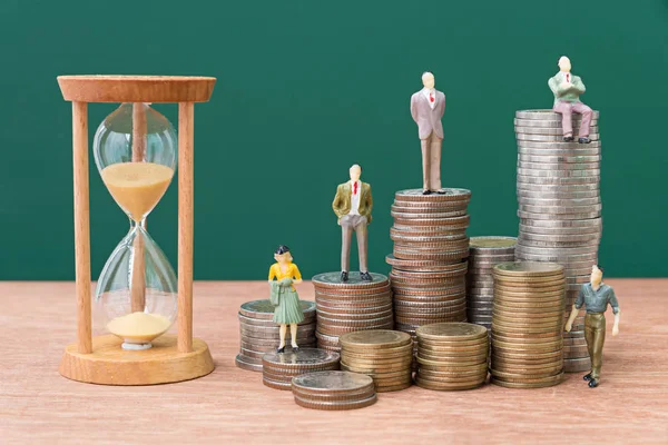 Miniature people on stack of coins with sand glass — Stock Photo, Image