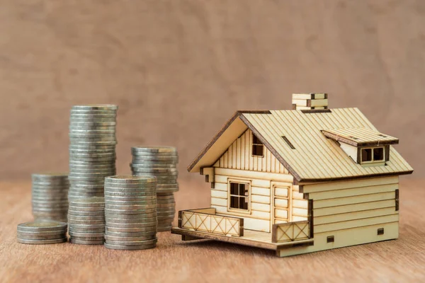 Pila de monedas y modelo de casa sobre fondo de madera marrón —  Fotos de Stock