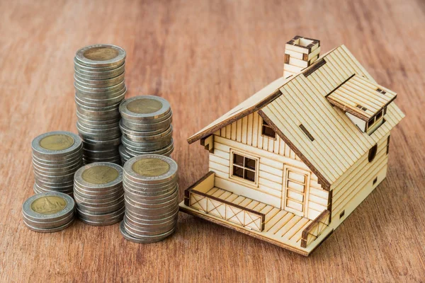 Pila de monedas y modelo de casa sobre fondo de madera marrón —  Fotos de Stock