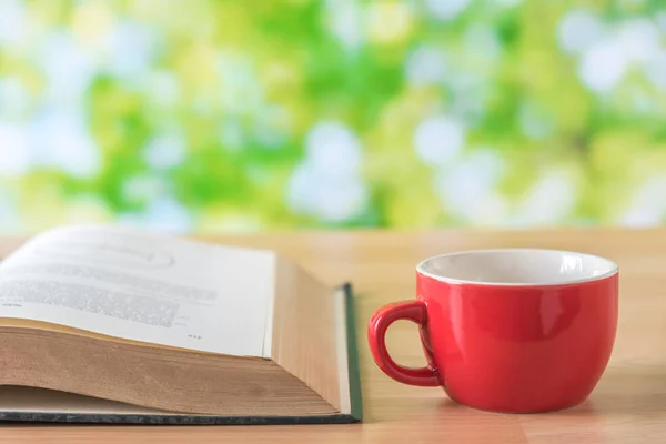 Tazza di caffè rosso su tavolo di legno con sfondo foglie verdi — Foto Stock