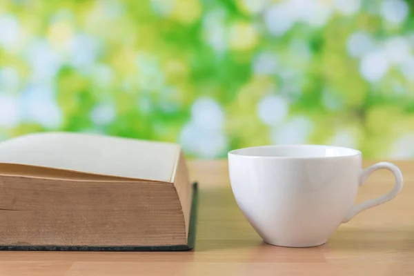 Taza de café blanco sobre mesa de madera con hojas verdes de fondo — Foto de Stock