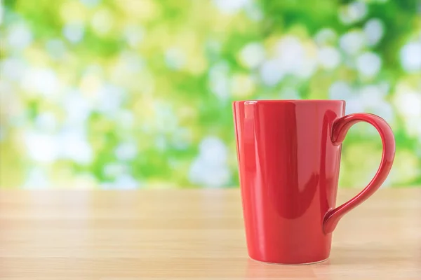 Чашка красного кофе на деревянном столе с зелеными листьями фона — стоковое фото