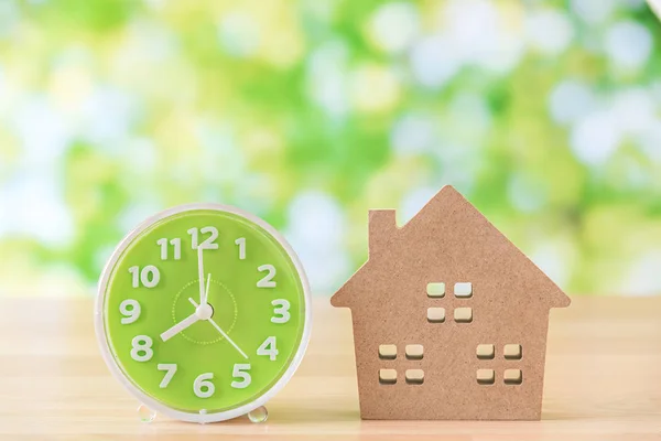 Green clock and house model on wooden table — Stock Photo, Image