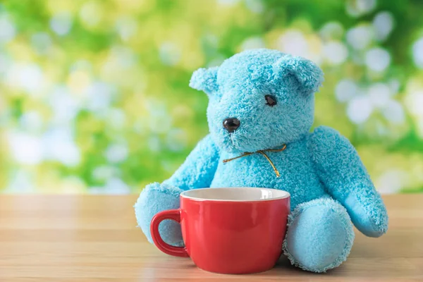 Blaubärpuppe sitzt auf Holztisch mit roter Kaffeetasse und g — Stockfoto