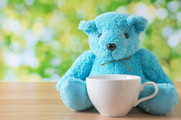 Blaue Bärenpuppe sitzt auf Holztisch mit weißer Kaffeetasse und — Stockfoto