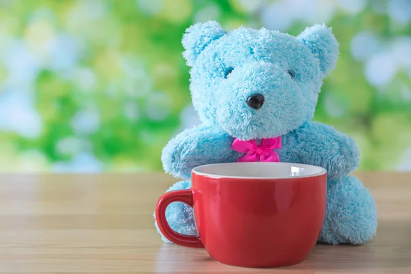 Blaubärpuppe sitzt auf Holztisch mit roter Kaffeetasse und g — Stockfoto