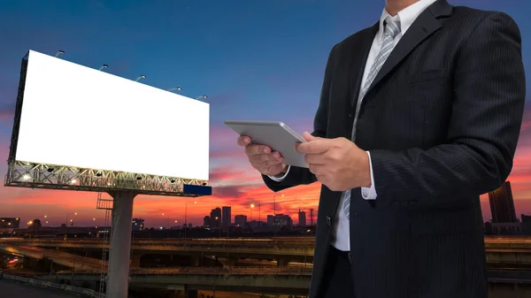 Businessman using phone or tablet with blank billboard at twilig — Stock Photo, Image