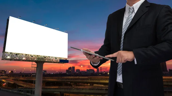 Businessman using phone or tablet with blank billboard at twilig — Stock Photo, Image