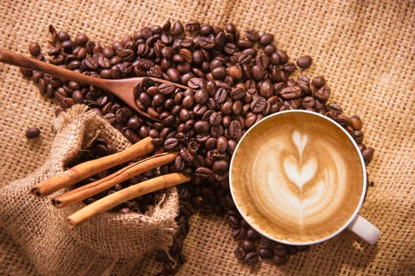 Чашка белого кофе и жареные кофейные зерна вокруг — стоковое фото