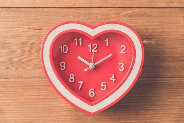 red heart clock on wood table , vintage tone