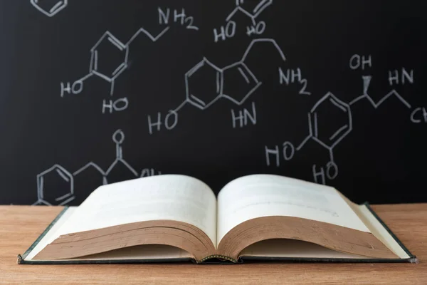 Buku terbuka di atas meja kayu dengan rumus sains di backgrou hitam — Stok Foto
