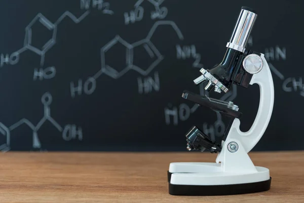 Microscopio sobre mesa de madera con fórmula científica sobre fondo negro — Foto de Stock
