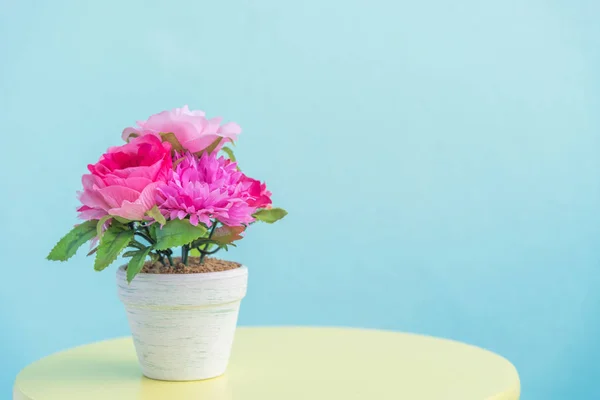 Искусственный цветочный горшок на деревянном столе и синем фоне стены — стоковое фото