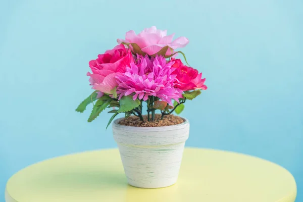 Maceta de flores artificiales sobre mesa de madera y fondo de pared azul —  Fotos de Stock