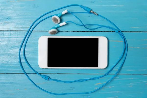 Mobilní telefon a modrá sluchátka na modrém pozadí — Stock fotografie