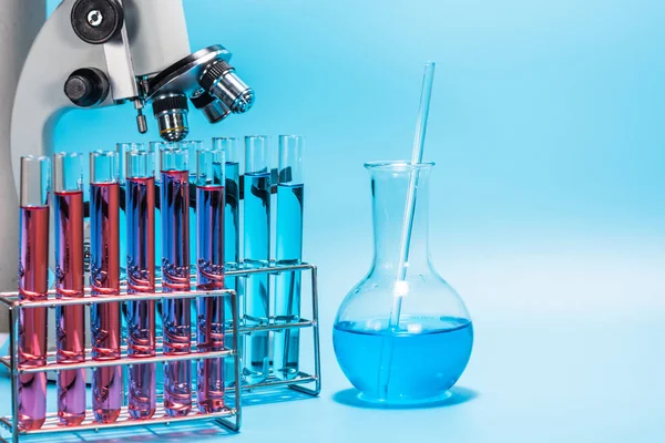 Microscópio e tubo de ensaio de laboratório em fundo azul claro, s — Fotografia de Stock