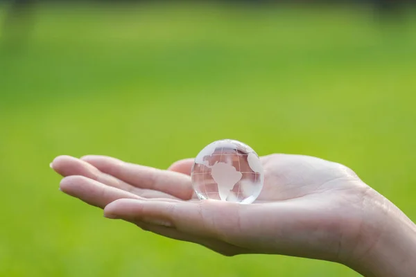 Üveg globe a nő kezét a zöld fű háttér — Stock Fotó