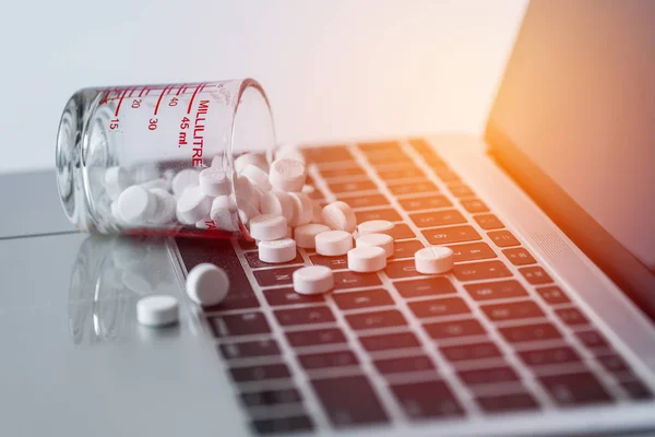 White pills splash out from measuring cup on laptop computer bac — Stock Photo, Image