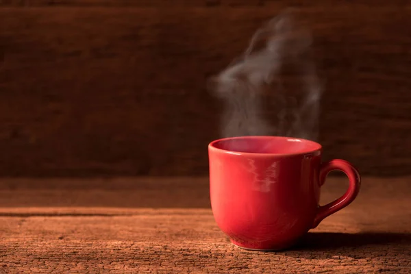 red coffee cup with smoke stream on wooden table under moring