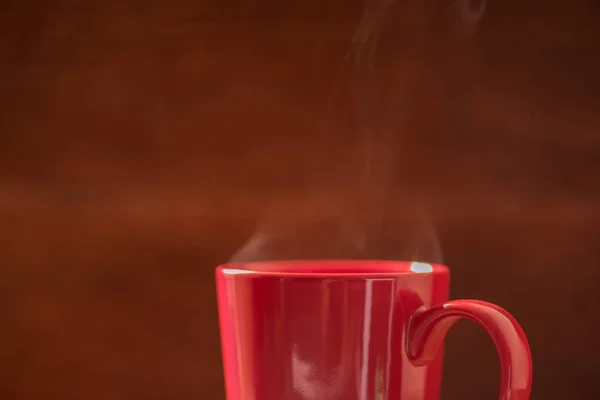 red coffee cup with smoke stream on wooden table under moring