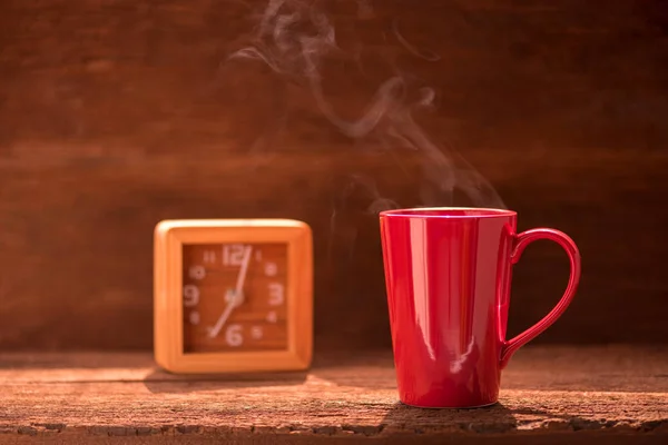 Röd kaffekopp med rök stream och klockan på träbord — Stockfoto