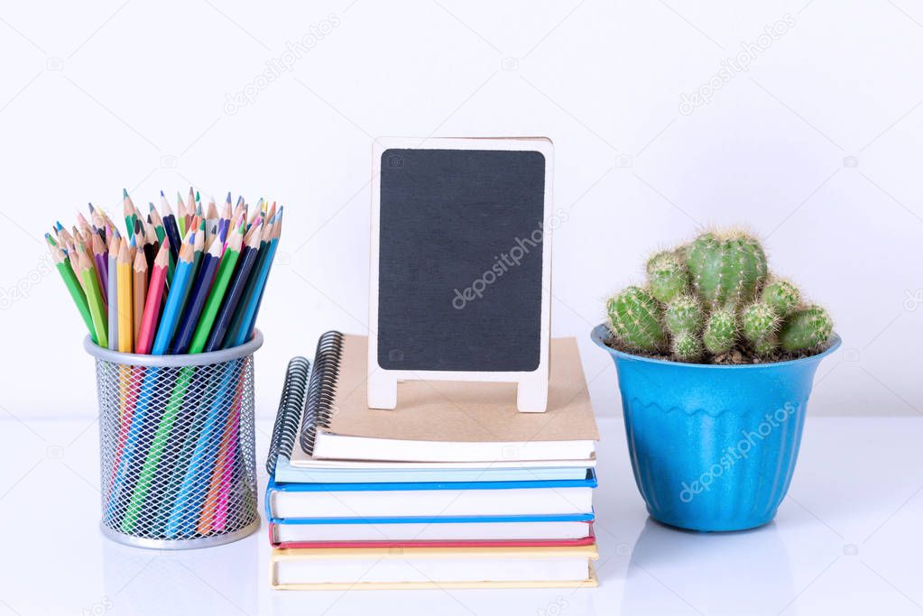 pencil box on book stack and flower pot on white table