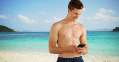 Beyaz adam sahilde metin iletilerini okumak için akıllı telefon kullanarak yüzmek şort giymiş.