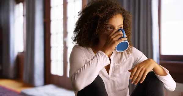 Black woman sitting alone at home with a cup of coffee