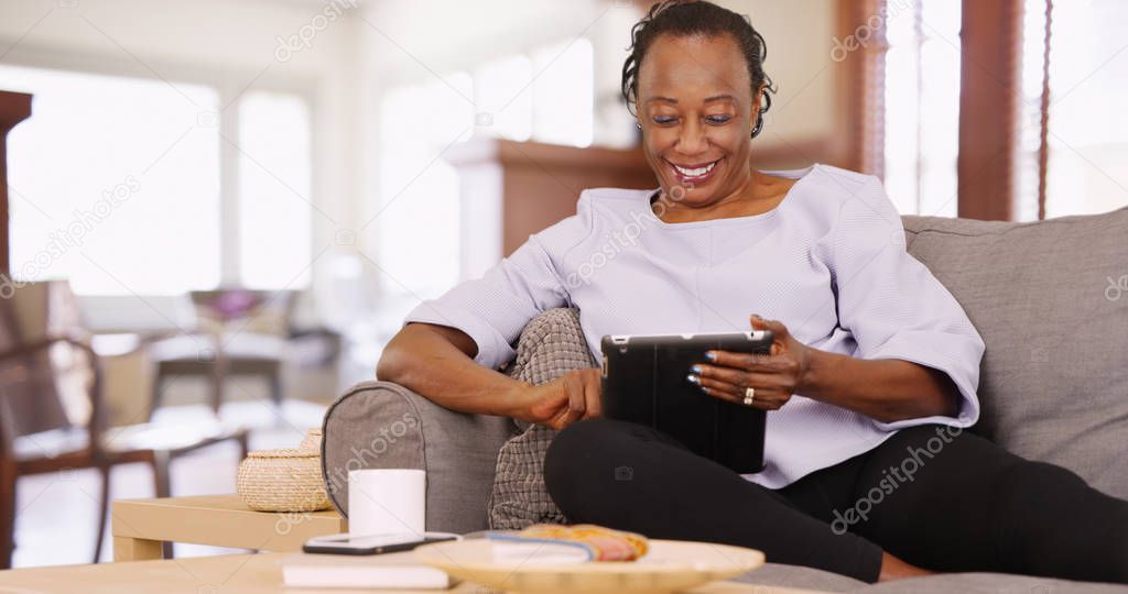 An elderly black woman uses her tablet while relaxing on the couch