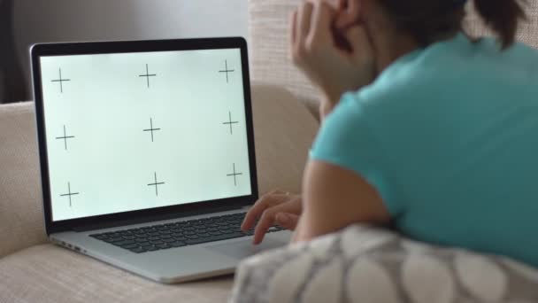 Женщина лежит на диване и работает на ноутбуке — стоковое видео