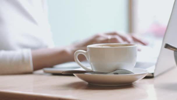 Женщина печатает за ноутбуком и пьет кофе — стоковое видео