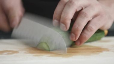 Genç adam Şef önden görünümü üzerinde kurulu kesme bıçağı ile ofgreen organik salatalık ince dilimler kesip.