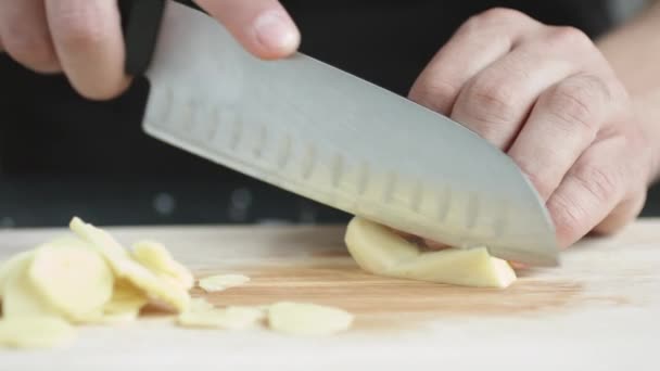 Framifrån av ung man kocken skär tunna skivor av en bit ingefära med kniv på skärning av styrelsen. — Stockvideo