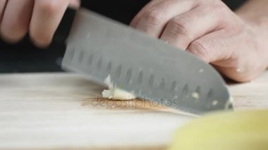 Yong adam aşçı önden görünümü üzerinde kurulu kesme bıçağı ile sarımsak ince dilimler kesip.