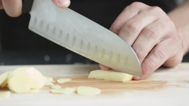 Vue de face du jeune chef coupé en fines tranches d'un morceau de gingembre avec couteau sur planche à découper . — Video
