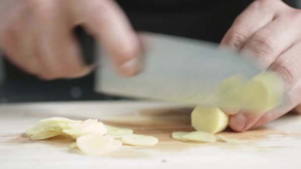 Vooraanzicht van jongeman chef Snij dunne plakjes van een stukje gember met mes op cutting Board. — Stockvideo