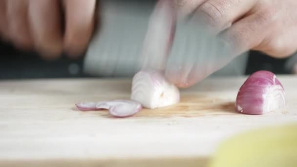 Vooraanzicht van yong man kok Snij dunne plakjes rode ui met mes op cutting Board. — Stockvideo