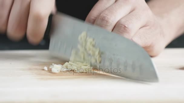 Vooraanzicht van yong man kok Snij dunne plakjes knoflook met mes op cutting Board. — Stockvideo