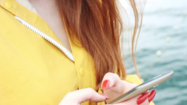 Жінка дивиться щось по телефону на узбережжі моря . — стокове відео
