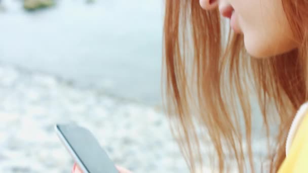 Vrouw op zoek iets op de telefoon aan de kust van de zee. — Stockvideo