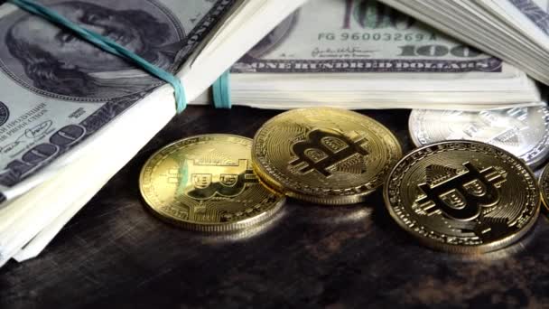 Monedas de bitcoin en billetes de cien dólares billetes en lotes gira en el escritorio grunge oscuro — Vídeo de stock