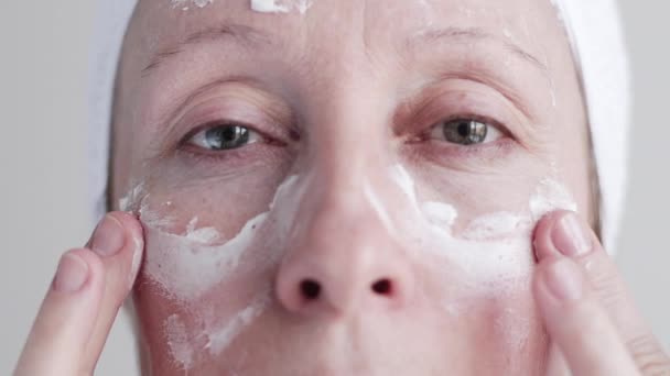 Caucásica mujer de mediana edad aplicando crema a su cara . — Vídeos de Stock