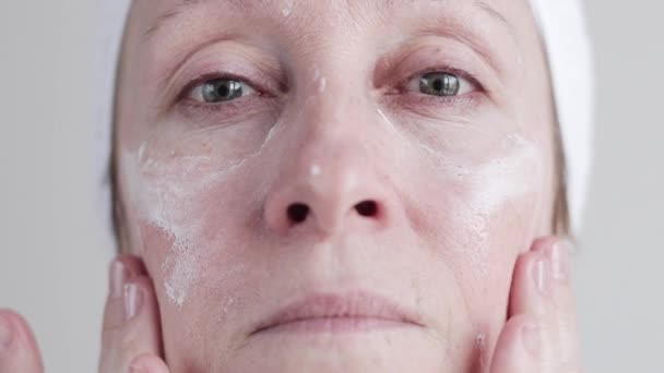 Кавказький середині вік жінки, застосовуючи крем на її обличчі. — стокове відео