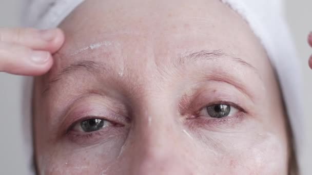 Kaukasische midden leeftijd vrouw crème op haar gezicht toe te passen. — Stockvideo