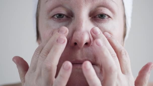年齢の女性が彼女の顔にクリームを適用する半ば白人. — ストック動画