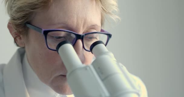 Женщина-ученый смотрит в микроскоп — стоковое видео