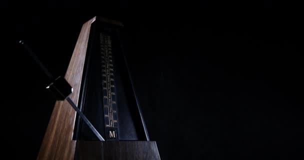 Metronome with golden pendulum beats slow rhythm on the dark background — Stock Video