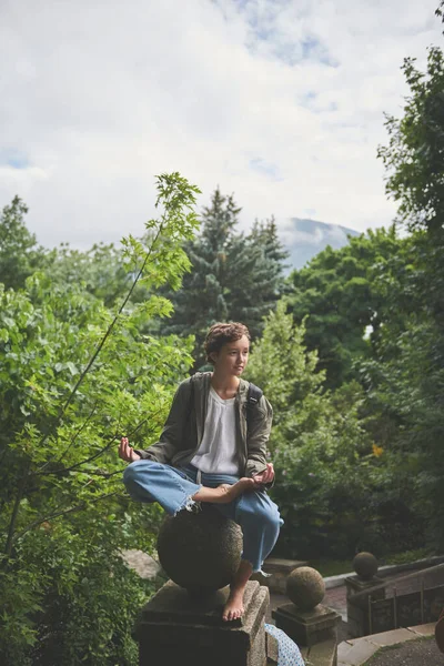 Dívka sedí v meditační držení těla na sochařské koule plotu v parku — Stock fotografie