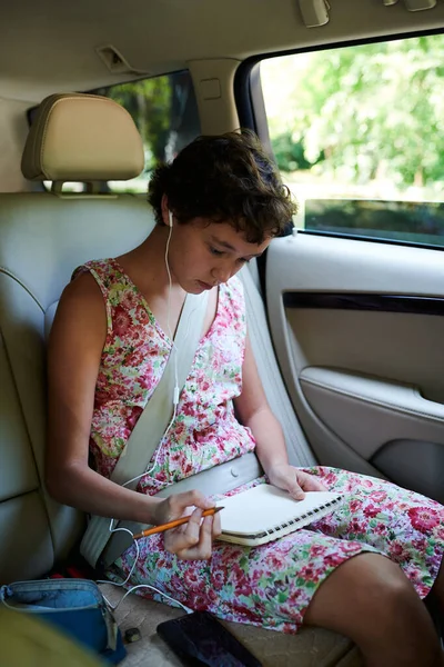 Задумчивая девушка рисует в альбоме эскизов на заднем сидении автомобиля — стоковое фото