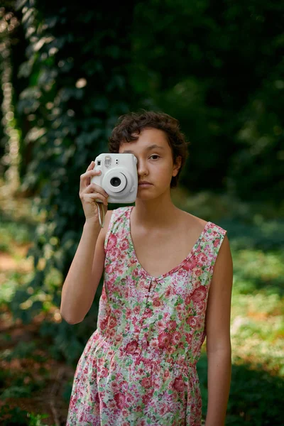 Smiling girl taking photo on instant camera in forest — Stock Photo, Image